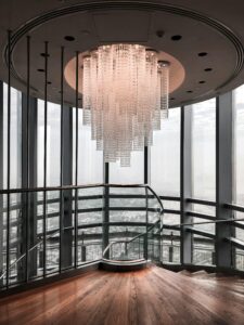 Elegant modern staircase interior featuring a large crystal chandelier and glass walls.